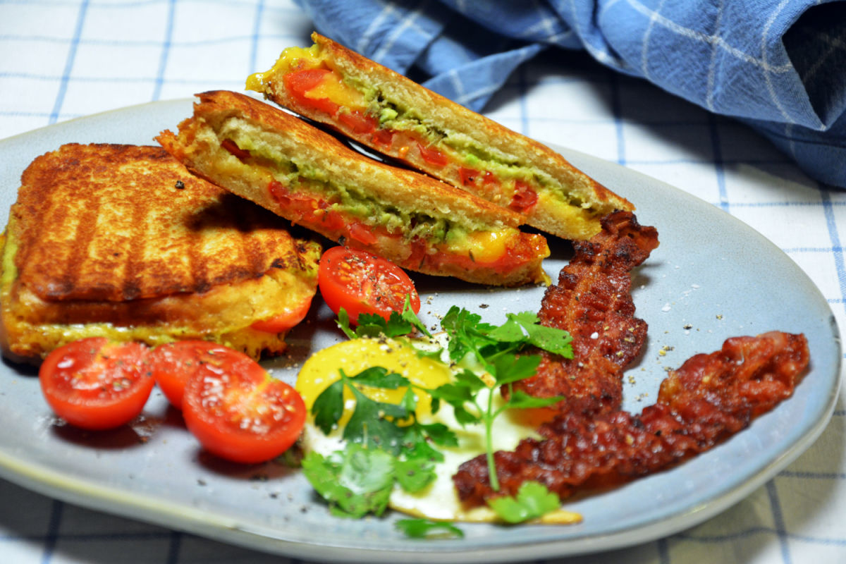 Smakfull avokado toast med speilegg og sprøstekt bacon servert på grovt brød