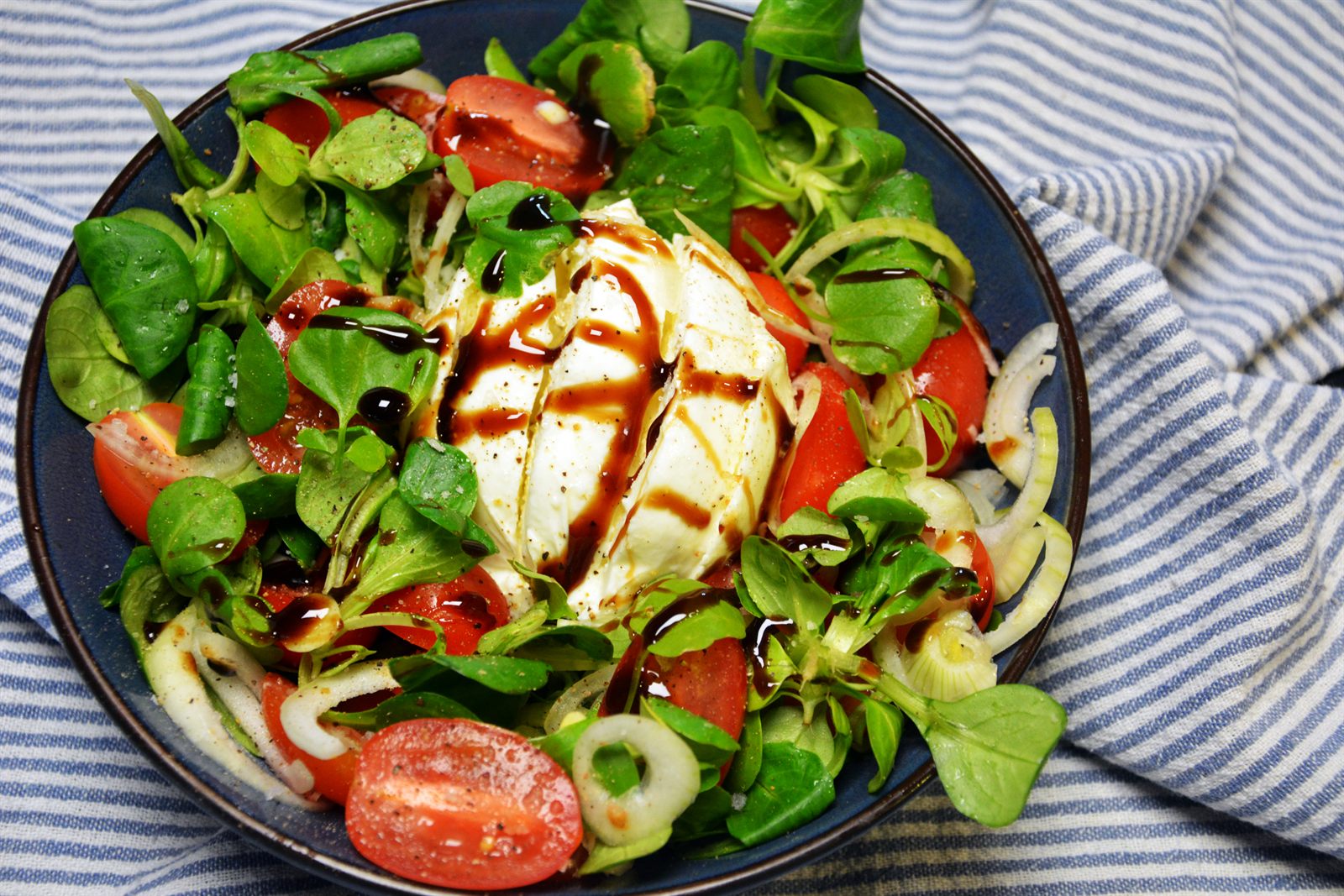Burrata salat med halve cherrytomater i flere farger, babyspinat, rødløk og balsamicoglaze på et fat