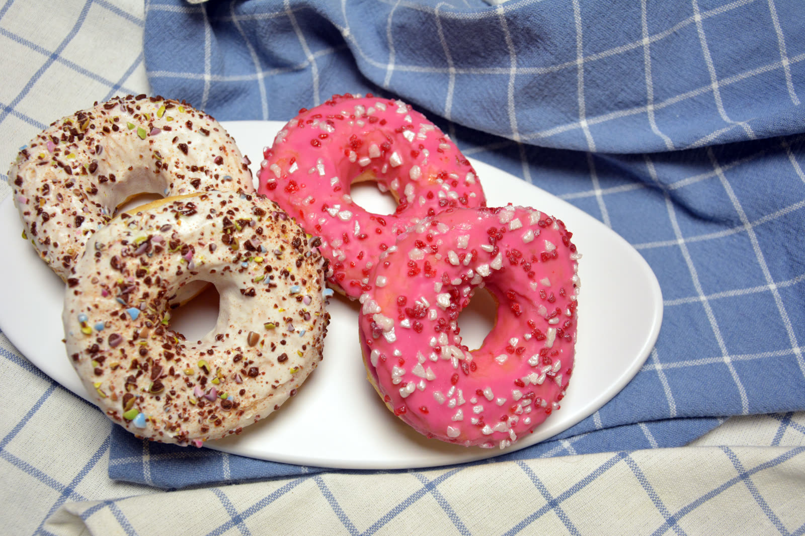 Hjemmelagde donuts med rosa og hvit melisglasur og fargerikt strøssel på et fat