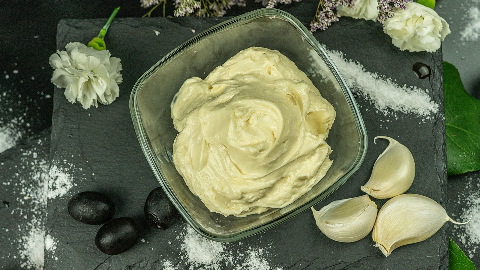 Hjemmelaget hvitløksdressing i en glasskål med hvitløksfedd ved siden av
