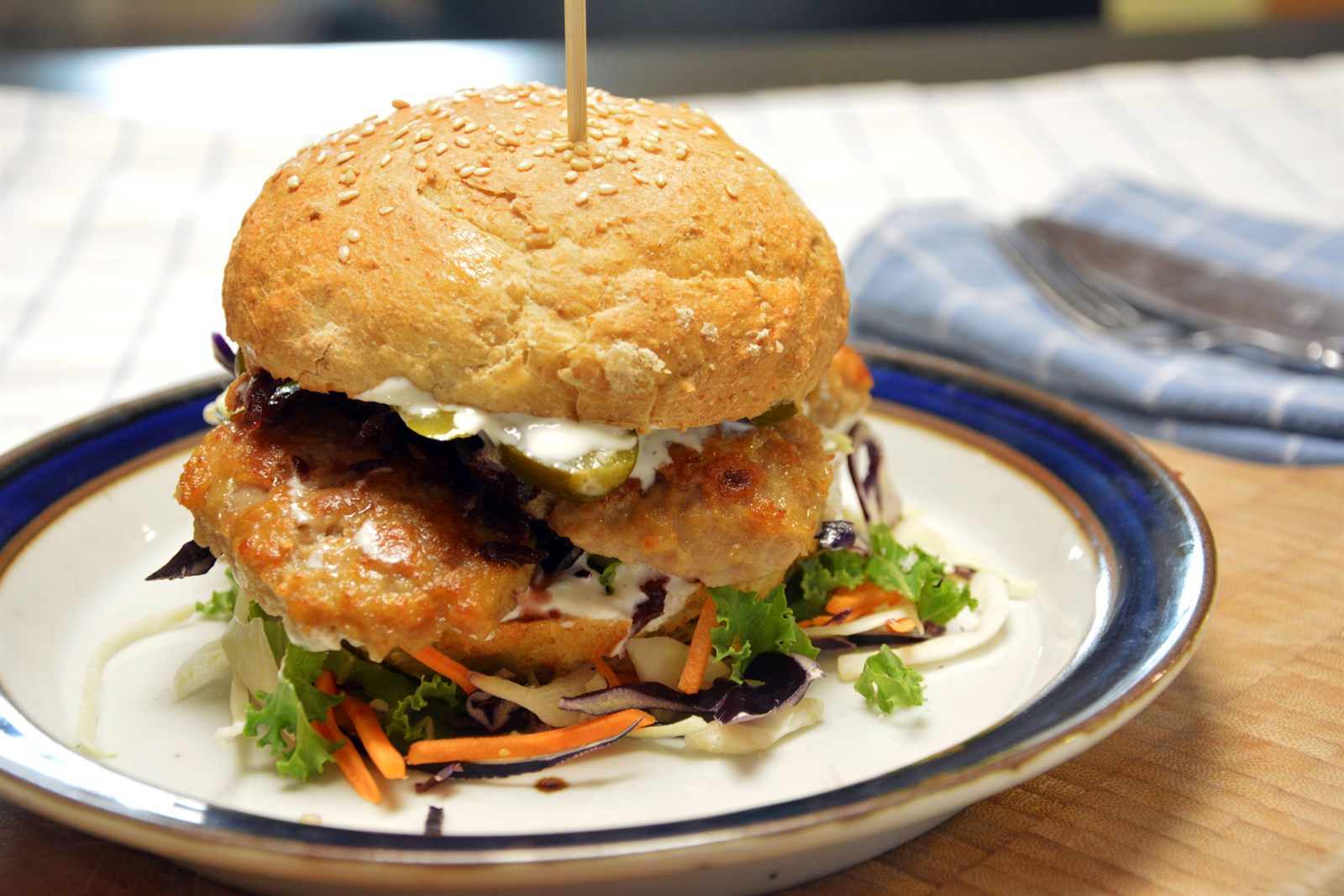 Karbonadesmørbrød i burgerbrød med kålsalat, rødkål og sylteagurk, holdt sammen av en grillpinne i tre