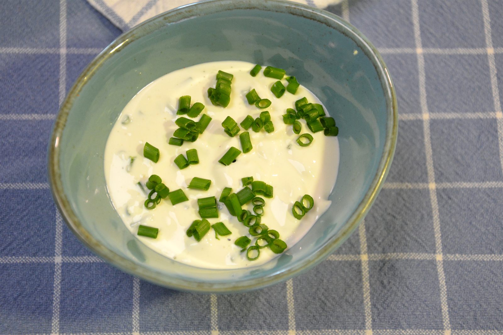 Rømmedressing med gressløk i en turkis skål på et blårutet kjøkkenhåndkle