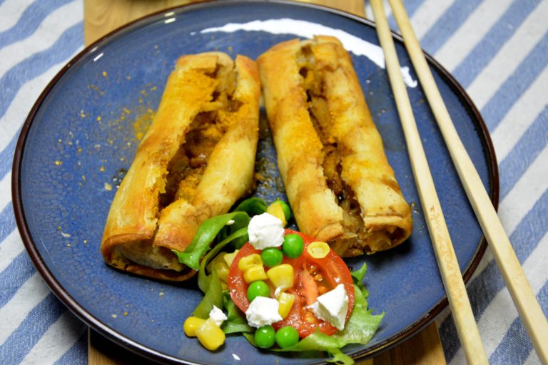 To sprø vårruller fra airfryer delt opp på en blå tallerken med en liten salat av tomat, mais, erter og fetaost