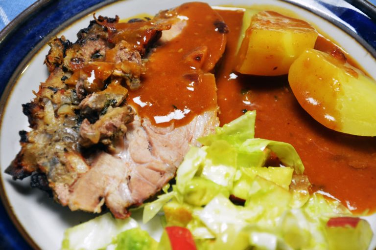 To skiver fylt svinenakke med mørkt soppfyll mellom skivene på en blåkantet tallerken, med brun saus, kokte poteter og grønn salat