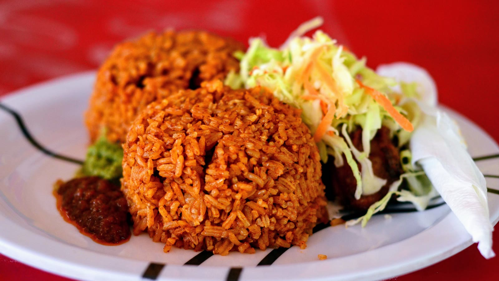 Jollof ris formet i en haug på tallerken med kålsalat og chilisaus på godtnoe.no